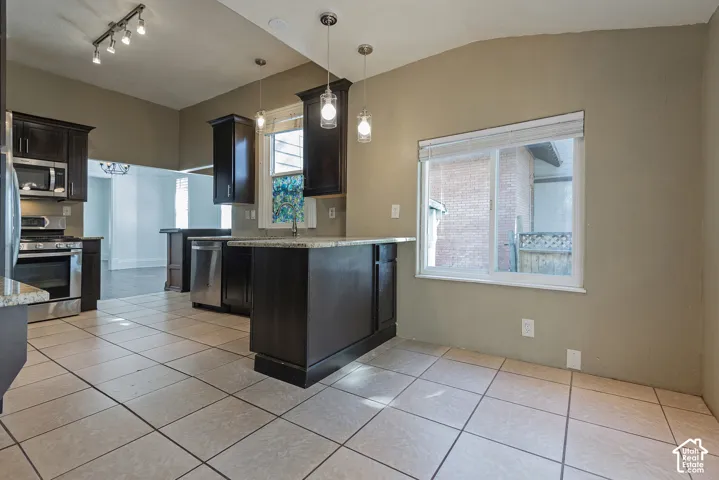 Kitchen with dark wood cabinetry, stainless steel appliances, light-toned tile flooring, and pendant lighting