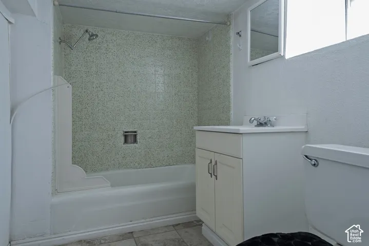 Bathtub with a shower fixture, wall-mounted mirror, white vanity with an integrated sink, and a toilet