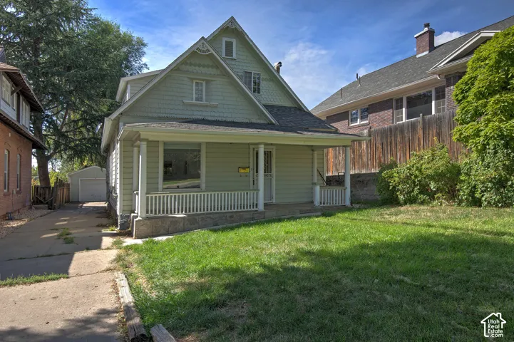 Gabled facade featuring shake siding, a covered porch with white railing, and a stone foundation