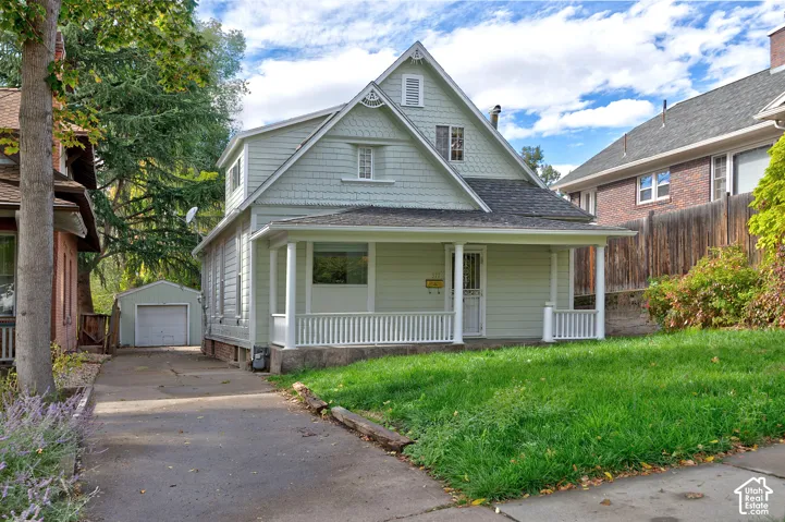 Two-story exterior featuring light green horizontal siding and decorative shingle accents, a covered front porch with white railing, and a detached single-car garage