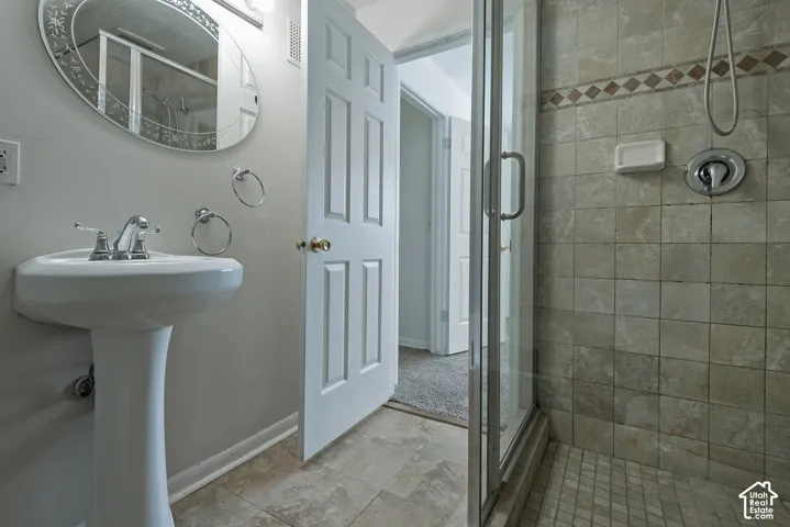 Pedestal sink with chrome faucet, oval mirror, walk-in shower with glass enclosure, tiled shower surround, and tiled flooring