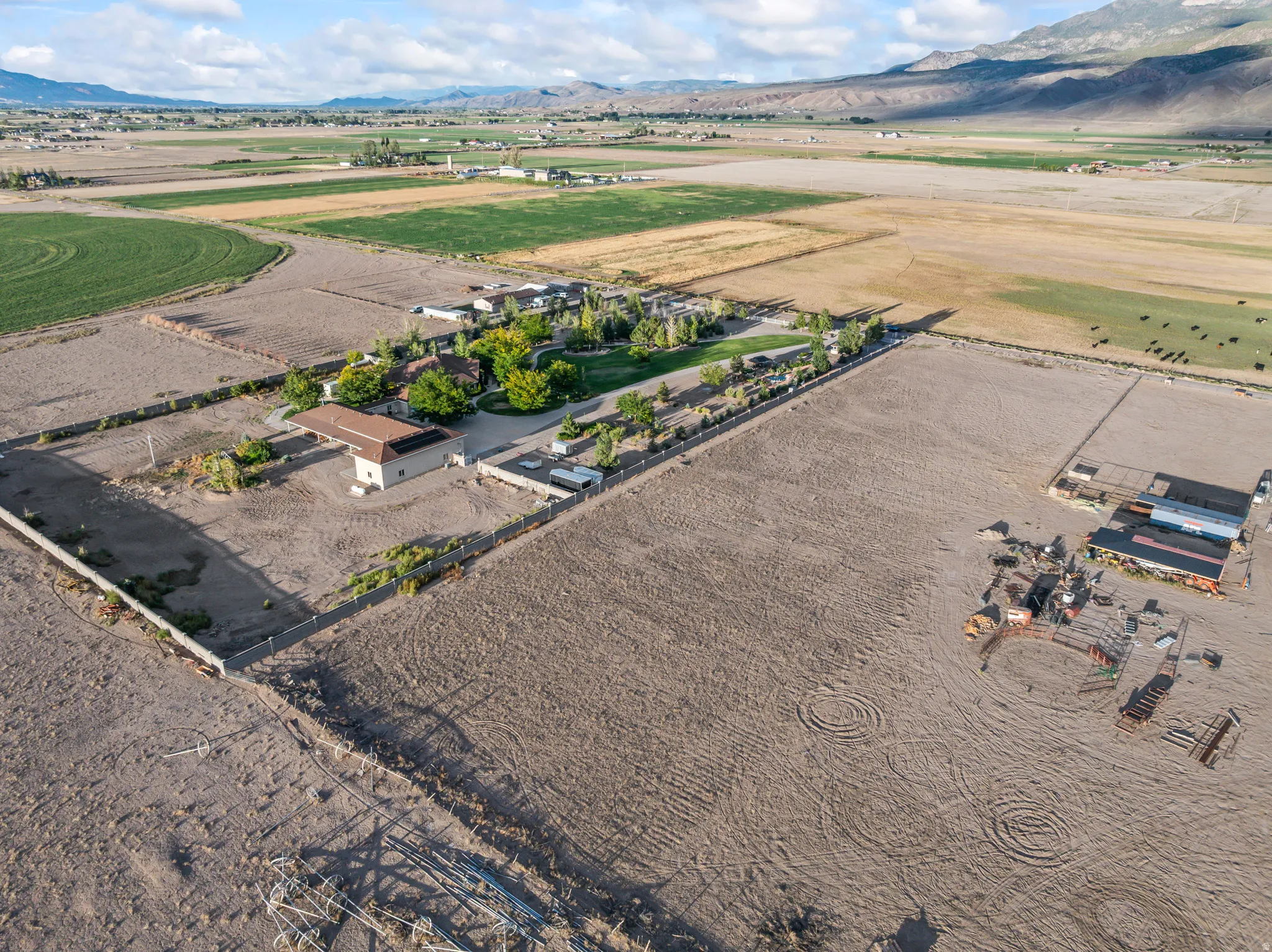 Expansive rural property featuring multiple structures, fenced perimeters, and surrounding open fields with distant mountain scenery