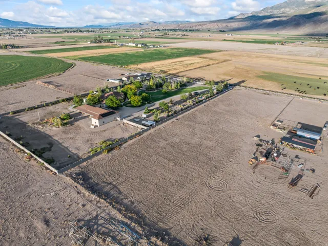 Expansive rural property featuring multiple structures, fenced perimeters, and surrounding open fields with distant mountain scenery