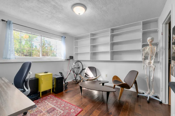 Room featuring wood-finish flooring, a large window, a ceiling-mounted light fixture, and extensive built-in shelving