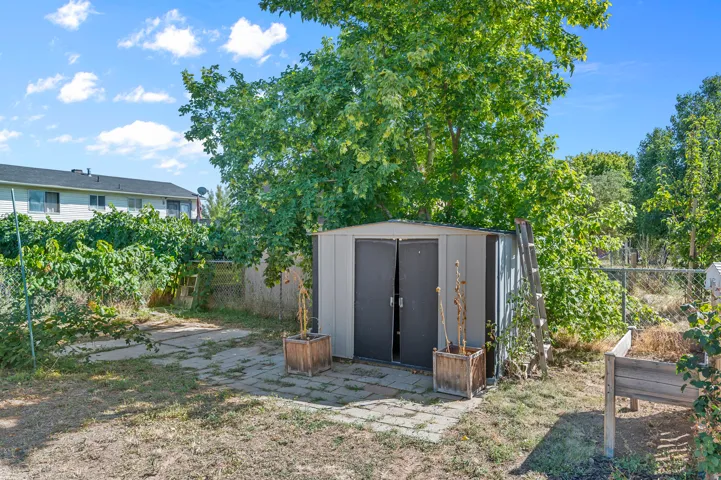 Detached storage shed with double doors, concrete paver landing, mature trees, and partial fencing