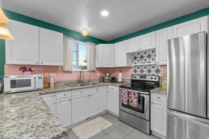 Kitchen featuring white cabinetry, granite countertops, stainless steel appliances, a pink subway tile backsplash, and decorative tile accent above the range