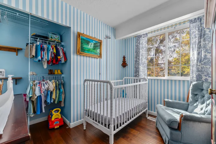 Room featuring wood-finish flooring, striped wall covering, and a window with a tree-lined backdrop