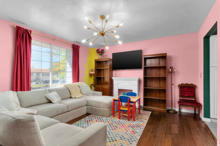 Spacious living area featuring wood-finish flooring, a contemporary ceiling light fixture, a window with natural light, and a decorative fireplace