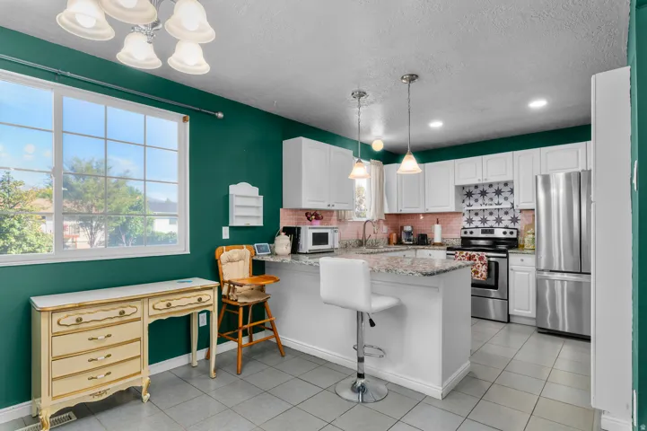 White cabinetry with granite countertops, stainless steel appliances, tile flooring, and a multi-pane window