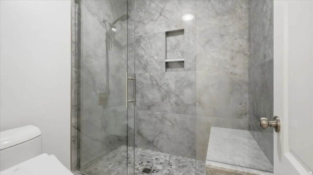 Glass-enclosed shower with stone-finish tile walls, built-in shelving, a shower bench, and pebble-style flooring