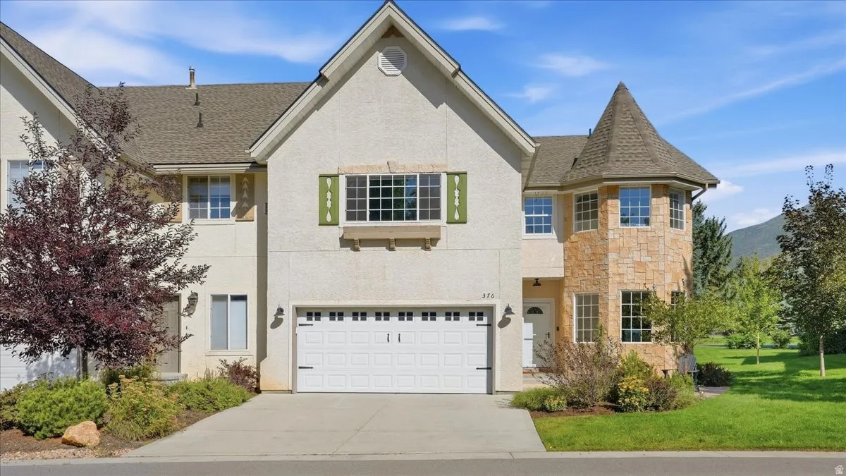 Exterior featuring a stone turret, stucco facade, attached garage, and landscaping