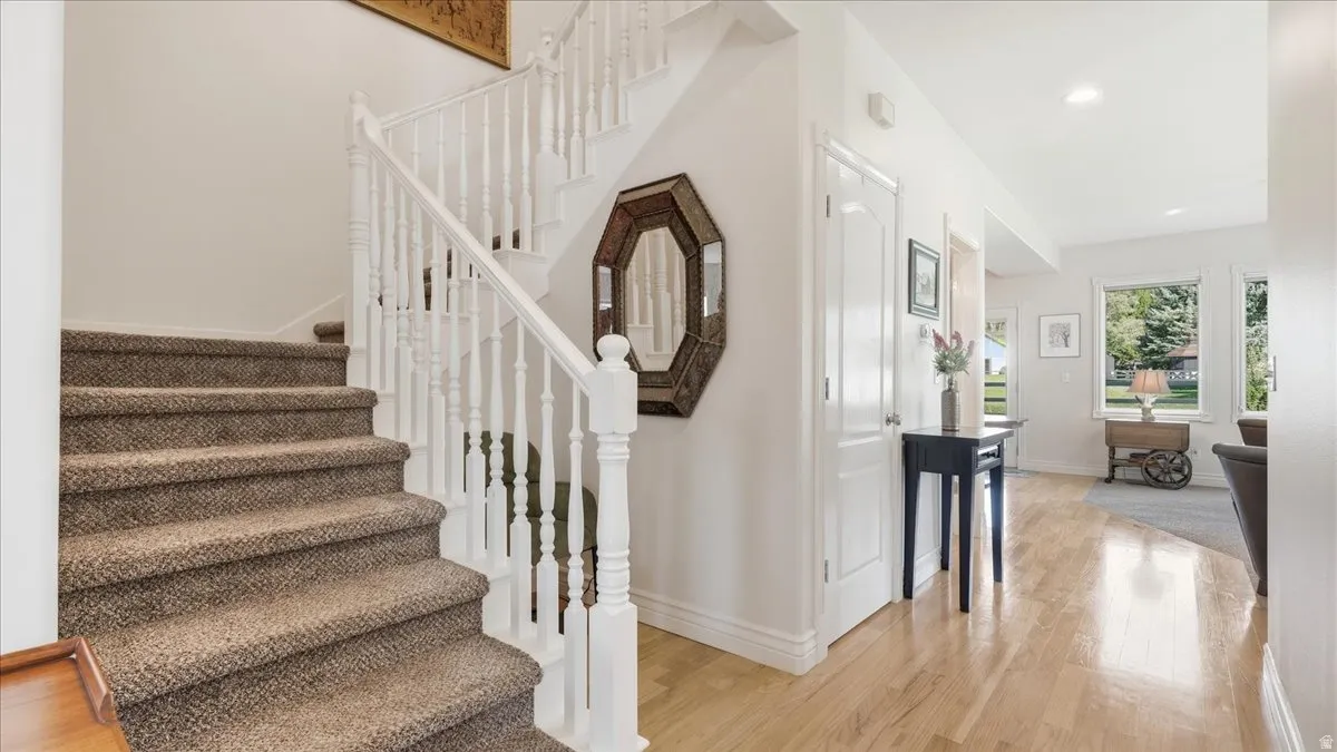 Hardwood flooring, painted white baseboards, and a staircase featuring carpeted treads and white balusters