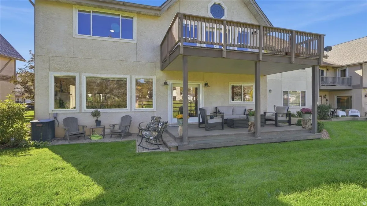 Expansive backyard featuring a manicured lawn, a lower-level patio, and an upper-level wood deck with railings
