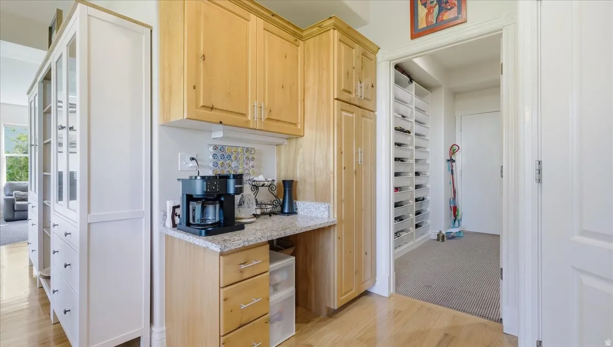 Built-in cabinetry with glass panel doors, wood-finish flooring, and a dedicated beverage station with stone-look countertop and decorative tile backsplash