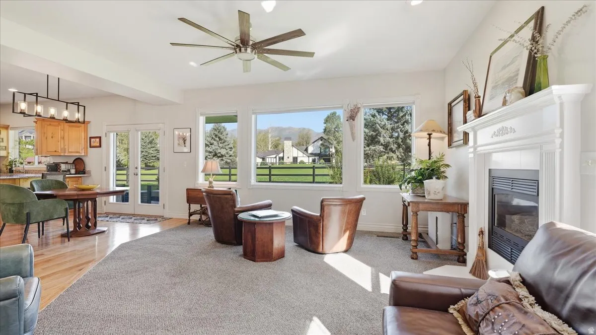 Formal fireplace with decorative mantel, multiple large windows, ceiling fan, wood-finish flooring, and French doors
