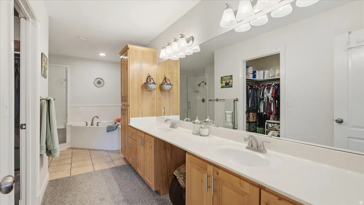 Double vanity with an integrated countertop, wood-finish cabinetry, a built-in soaking tub, a separate glass-enclosed shower, and a walk-in closet