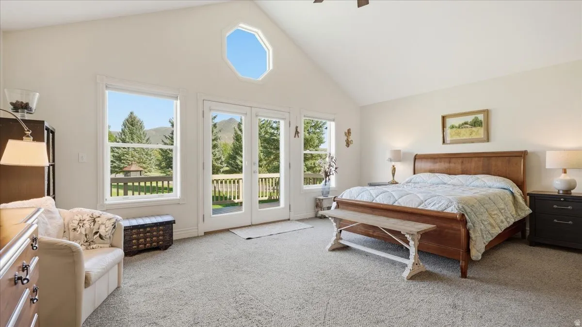 Vaulted ceiling with an octagonal window, French doors opening to a balcony, large picture window, and neutral carpeting