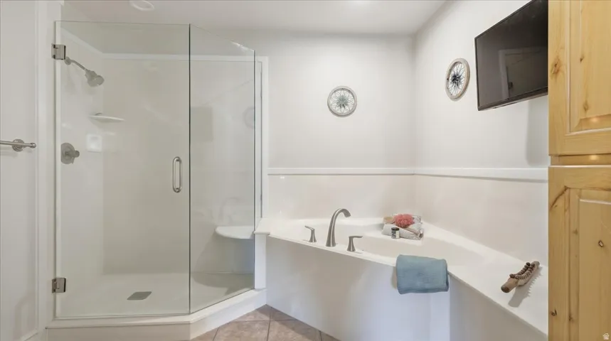 Enclosed glass shower with built-in seating, corner soaking tub with deck-mounted fixtures, and integrated wood cabinetry