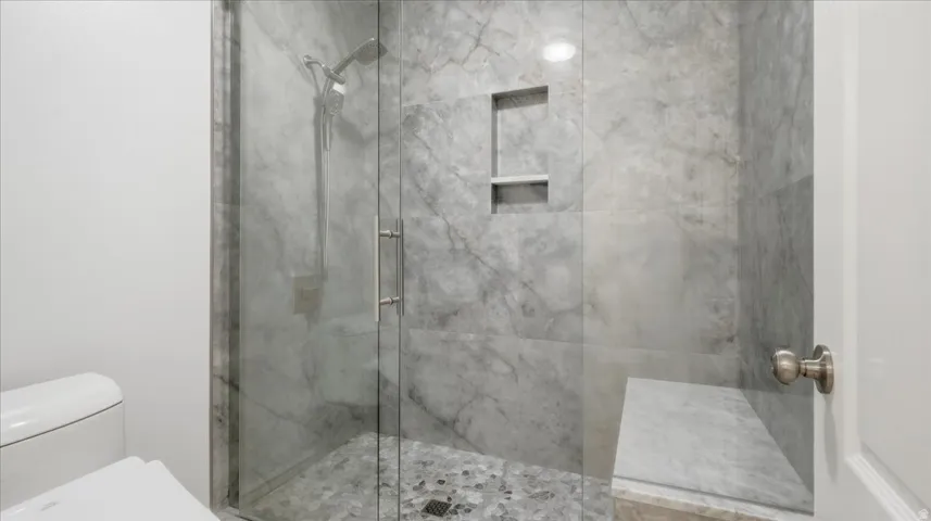 Glass-enclosed shower with stone-finish tile walls, built-in shelving, a shower bench, and pebble-style flooring