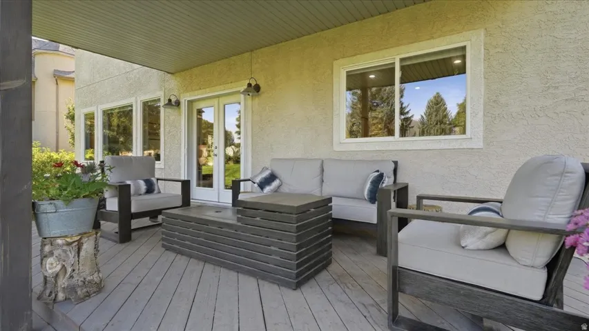 Covered outdoor patio with wood-finish decking, double French doors, and exterior wall sconces