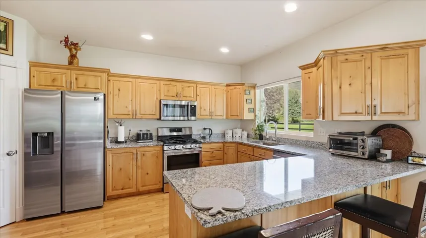 Kitchen featuring light wood cabinetry, stainless steel appliances, speckled stone countertops, and wood-finish flooring