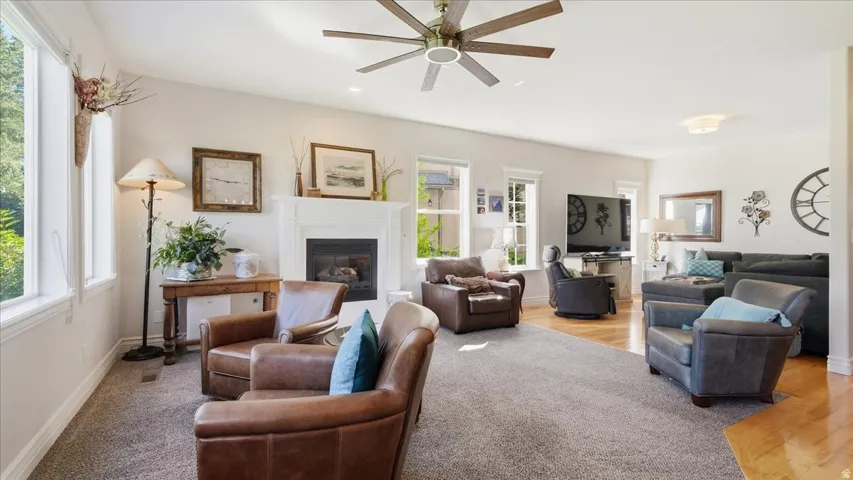Spacious living area featuring a fireplace with a white mantel, multiple windows, a ceiling fan, and recessed lighting