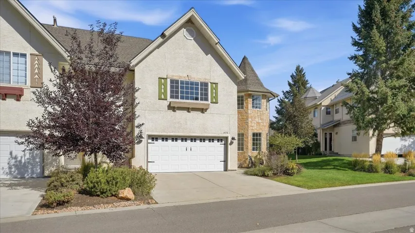 Stucco exterior with a peaked roofline, an attached two-car garage, and a stone-clad turret