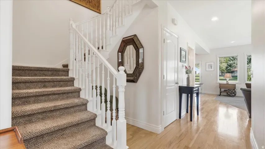Hardwood flooring, painted white baseboards, and a staircase featuring carpeted treads and white balusters