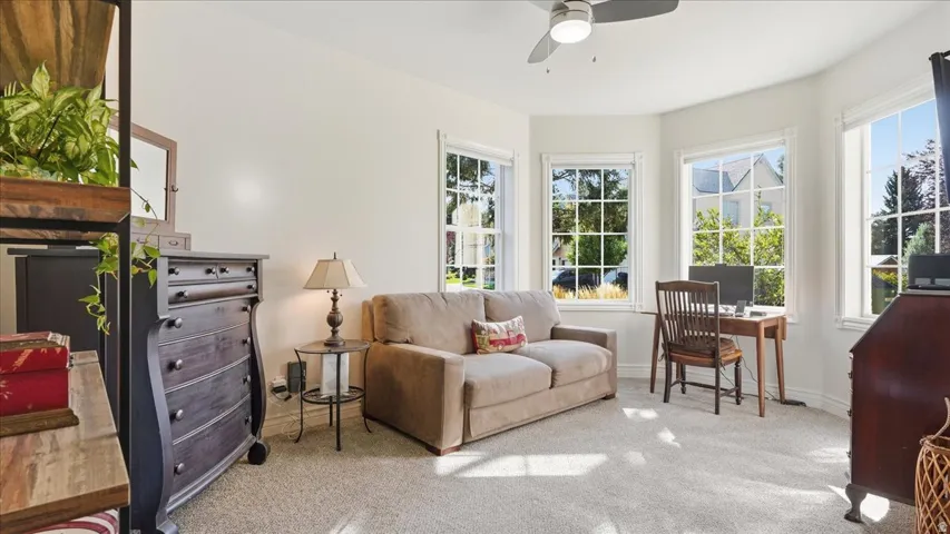 Bay window with multiple pane windows, ceiling fan, and light-toned carpeting