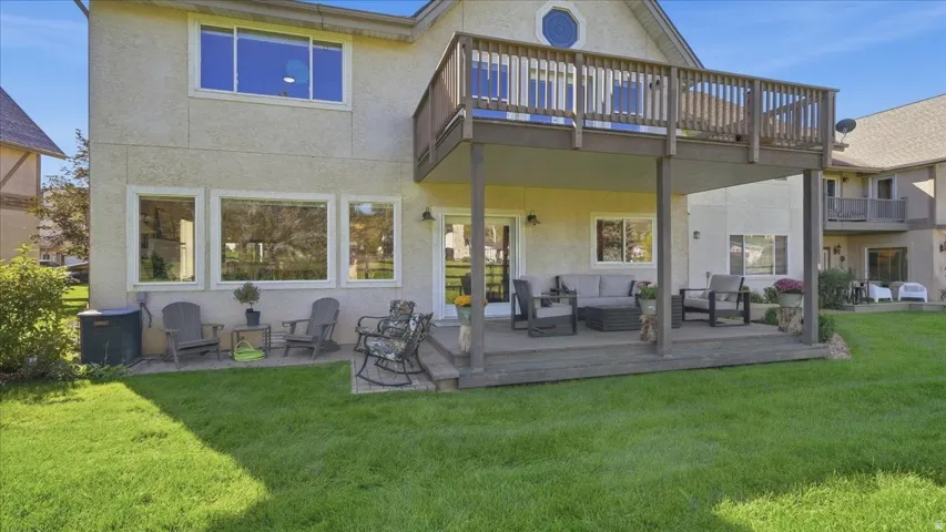 Expansive backyard featuring a manicured lawn, a lower-level patio, and an upper-level wood deck with railings