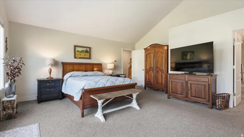 Vaulted ceiling with neutral wall tones, window with natural light, and carpeted flooring