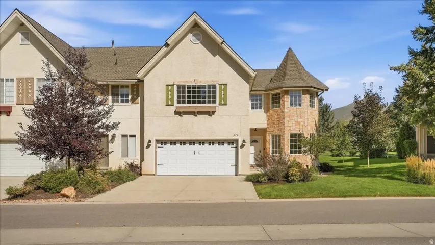 Stucco exterior featuring a stone turret, attached garage, and prominent gables
