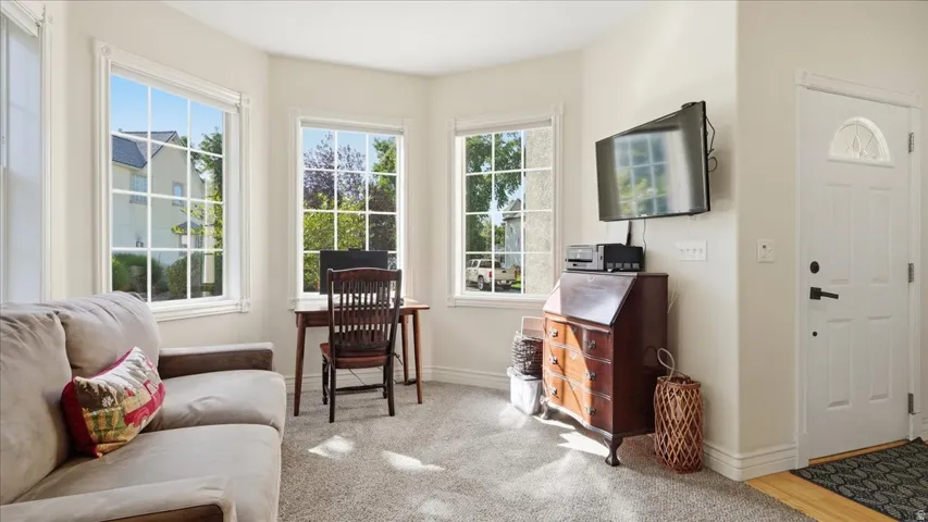 Well-lit interior with bay windows, neutral wall tones, carpeted flooring, and a paneled entry door with frosted glass