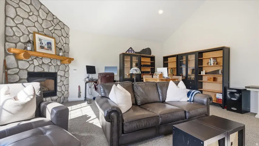 Stone-clad fireplace with a log mantel, vaulted ceiling, built-in shelving, and recessed lighting