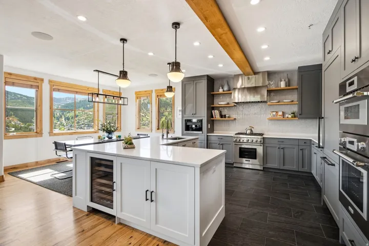 Gourmet kitchen with stainless steel appliances, custom cabinetry, a large center island with built-in wine cooler, wood-finish flooring, and exposed beam ceiling