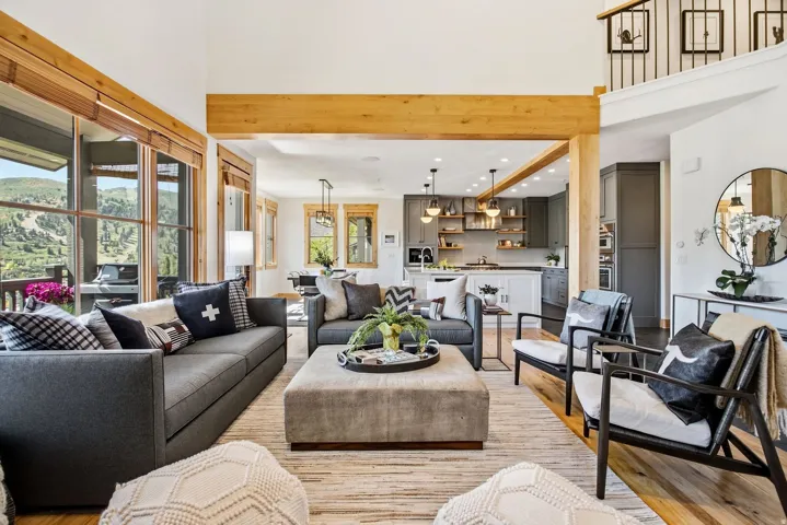 Open-concept living area featuring high ceilings, exposed wood beams, and large windows