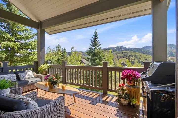Expansive covered deck featuring wood-finish flooring, sturdy wood railing, and structural columns, with a prominent mountain backdrop