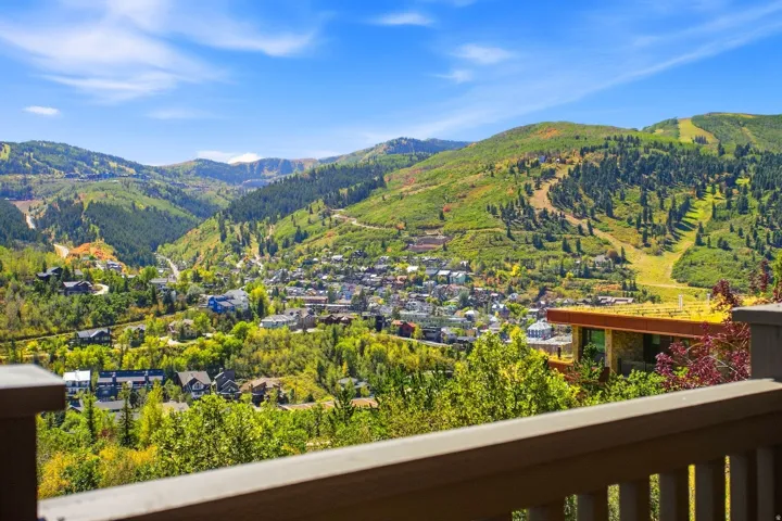 Expansive mountainous landscape with a community nestled in the valley, featuring verdant tree coverage and a clear blue sky