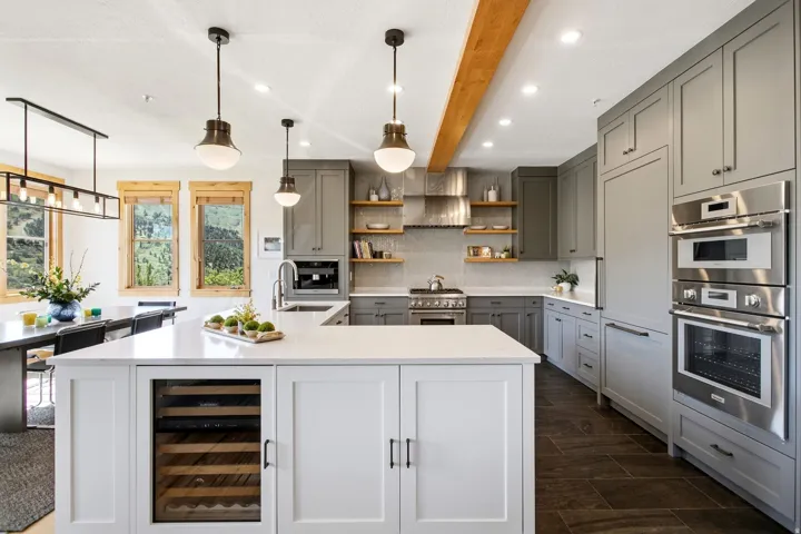 Bright kitchen featuring a substantial island with integrated beverage refrigerator, light gray cabinetry, built-in stainless steel appliances, and wood-finish ceiling beam
