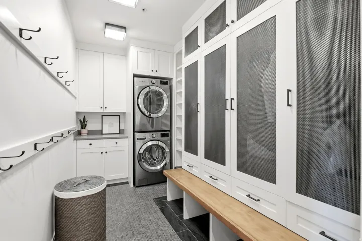 Laundry area featuring a stacked washer and dryer, built-in white cabinetry with a light-colored countertop, and a built-in wooden bench