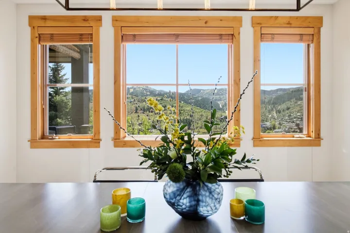 Wood-finish dining table with a linear chandelier and three windows featuring wood trim
