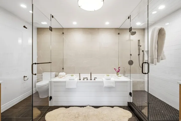 Full glass shower enclosure with dark bronze hardware, built-in soaking tub with shiplap-style surround, and large format wall tiling