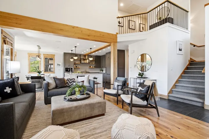 Open-concept living area featuring exposed wood beams, wood-finish flooring, and a carpeted staircase with a black metal railing