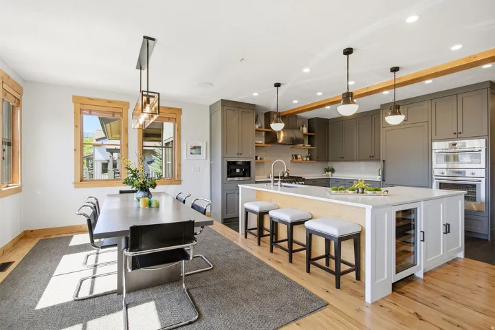 Wood-finish flooring, gray cabinetry, large kitchen island with integrated wine refrigerator, built-in stainless steel appliances, and wood-trimmed windows