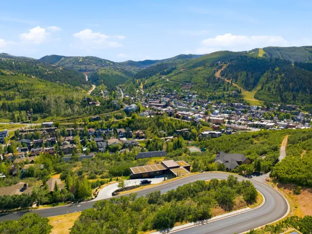 Paved roads winding through green hillsides, a distant town center with various buildings, and a mountainous backdrop with clearings