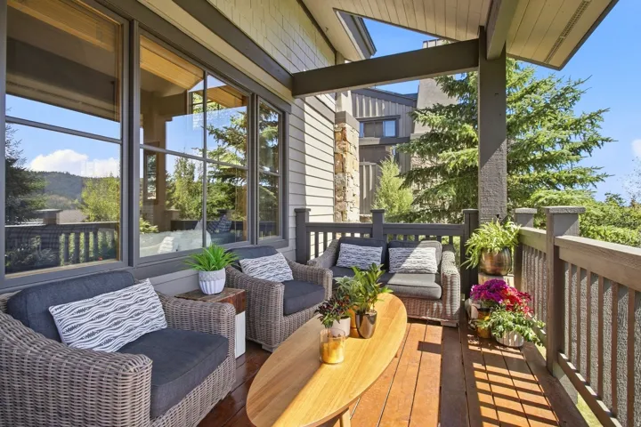 Covered outdoor deck with wood-finish flooring, dark wood railing, and multi-pane windows