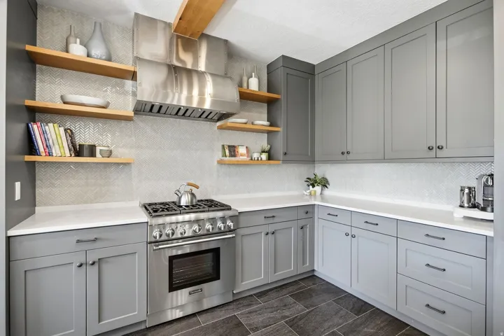 Gray shaker-style cabinetry with dark hardware, stainless steel range with matching range hood, white countertops, chevron pattern tile backsplash, and dark tile flooring