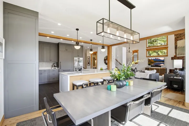 Expansive open-concept living space with exposed wood beams, a modern linear chandelier, and recessed lighting