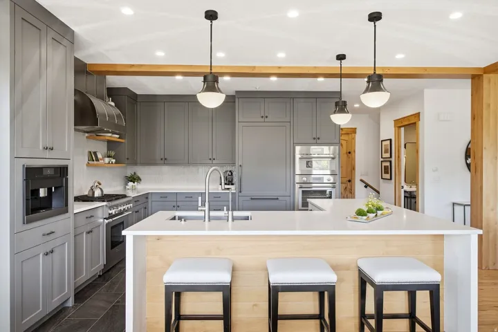 Contemporary kitchen featuring grey cabinetry, stainless steel appliances, a center island with countertop seating, a tile backsplash, and dark tile flooring