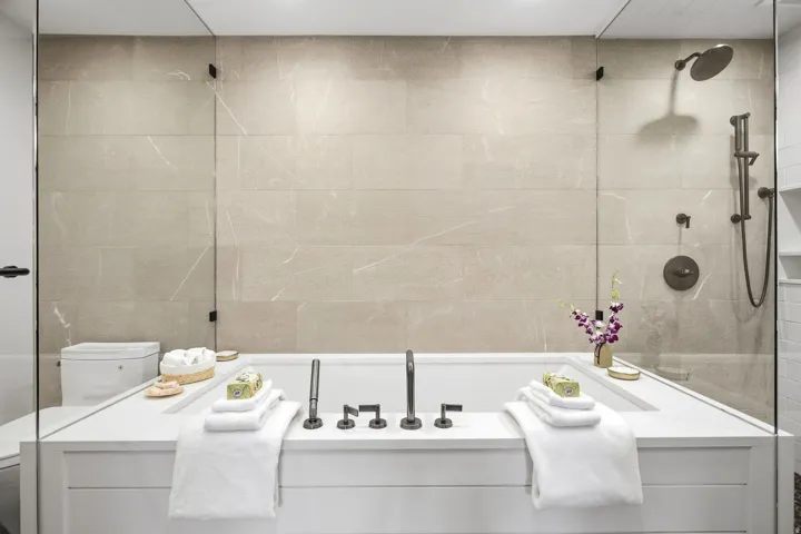 Built-in soaking tub with dark bronze fixtures, glass shower enclosure, shower panel with handheld spray, and large format wall tiling